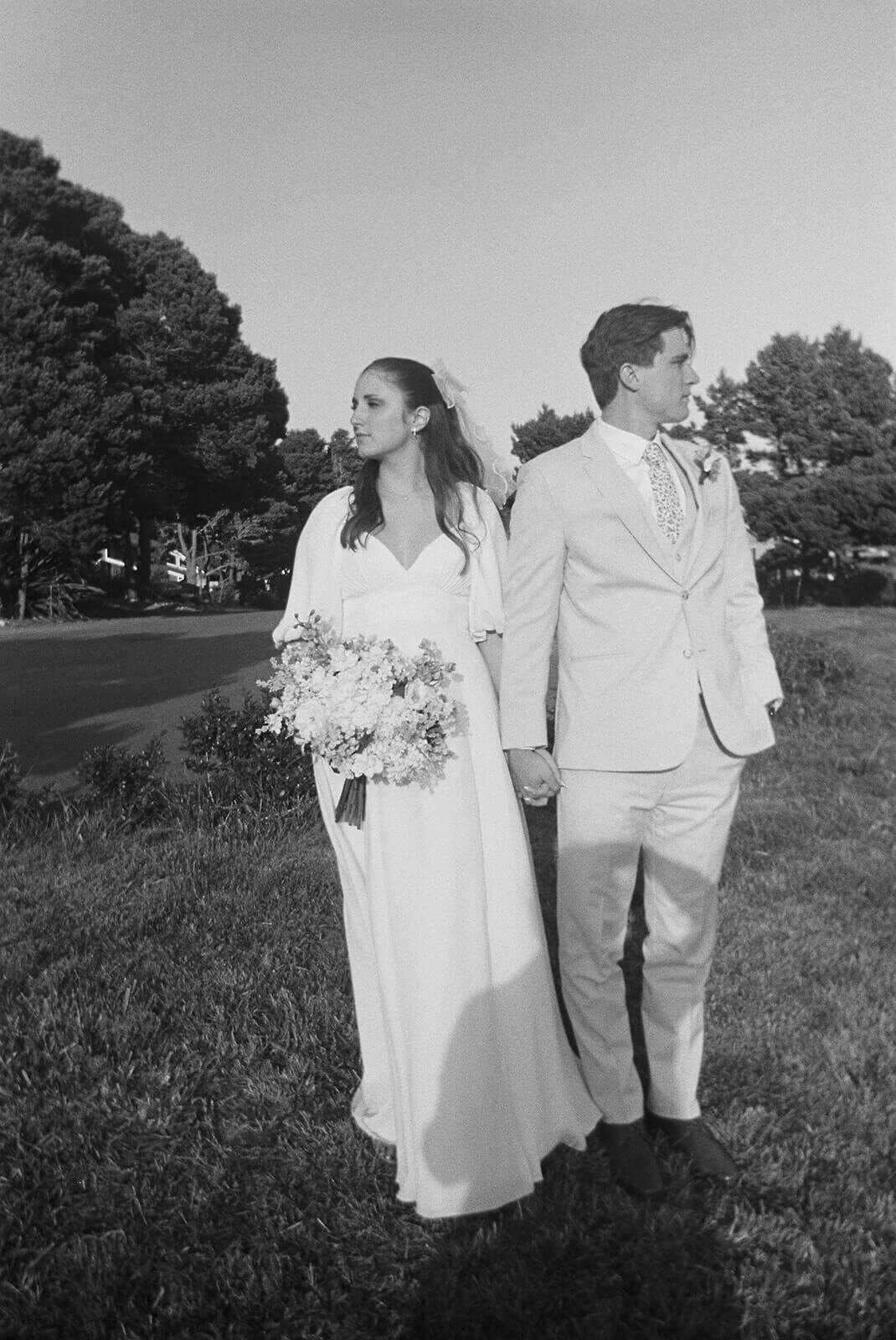 A black and white image of a bride and groom holding hands and looking away from each other.