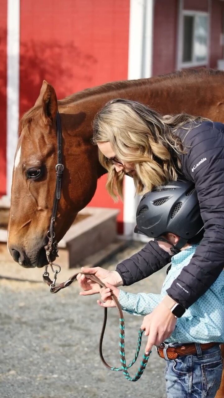 A riding instructor showing a young boy how to hold the reins of a chestnut pony, they are standing next to the pony