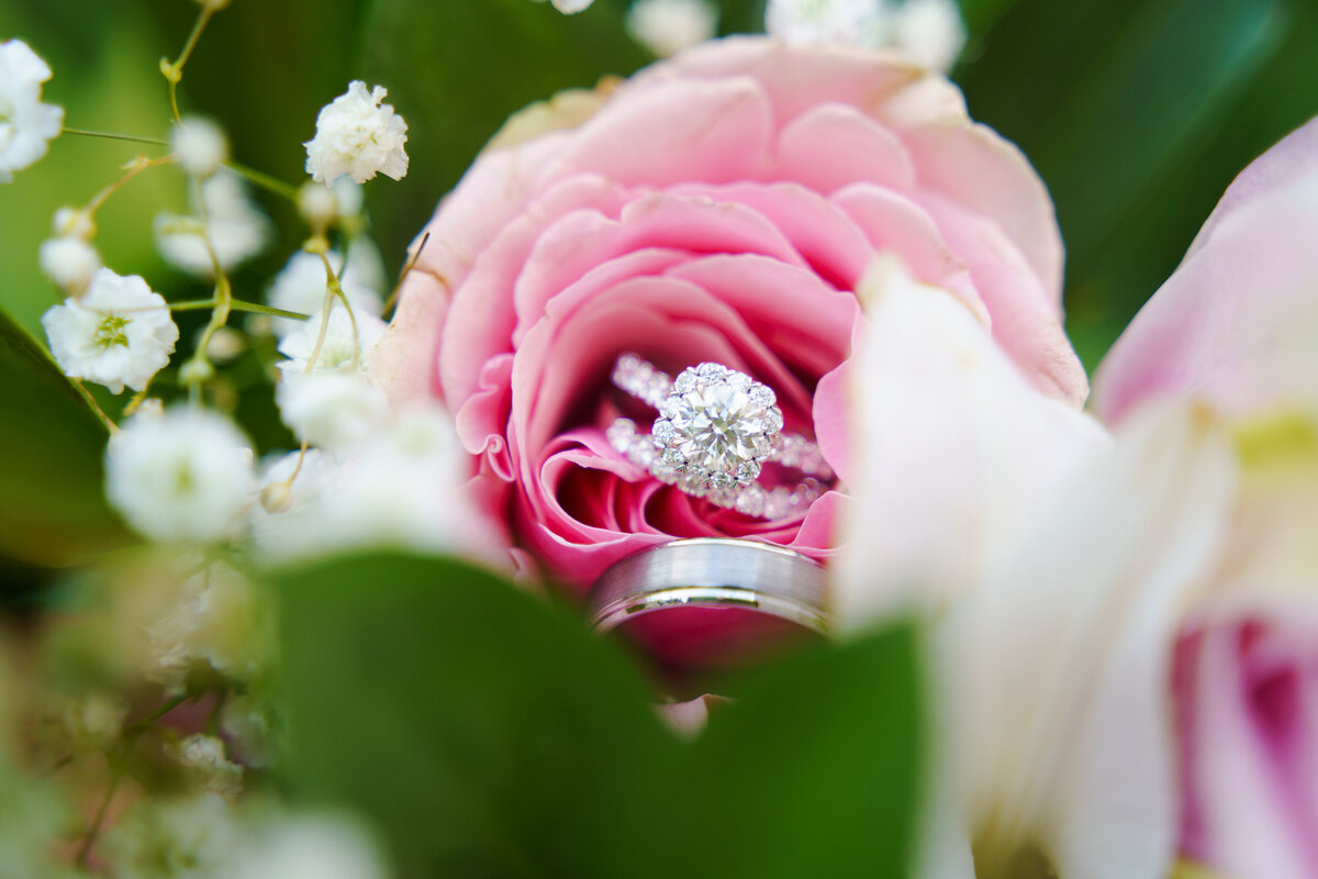 Beautiful wedding rings placed in between the petals of a pink rose in the bride's bouquet at a backyard wedding in Dublin, Ohio,