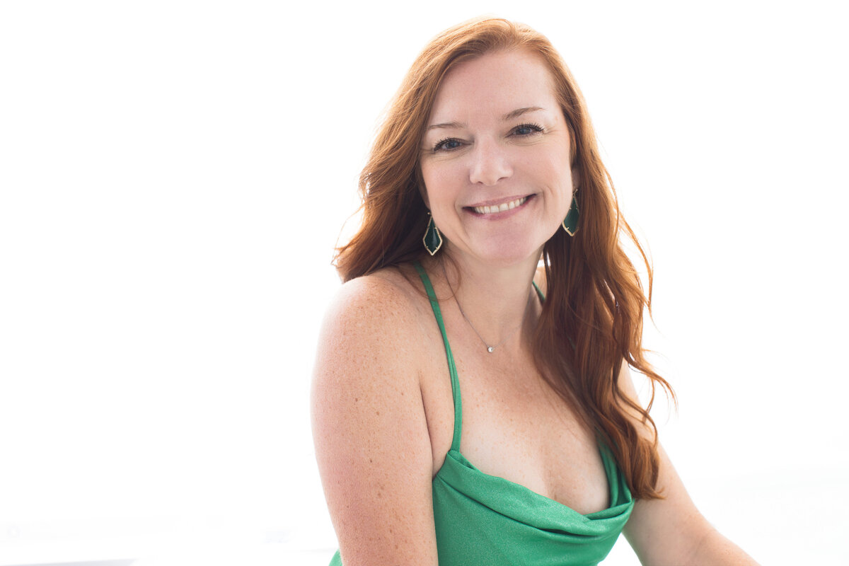 Cincinnati portrait photographer captures a radiant woman in a vibrant green dress, her red hair flowing gracefully. Her genuine smile and confident gaze exemplify the essence of modern elegance.