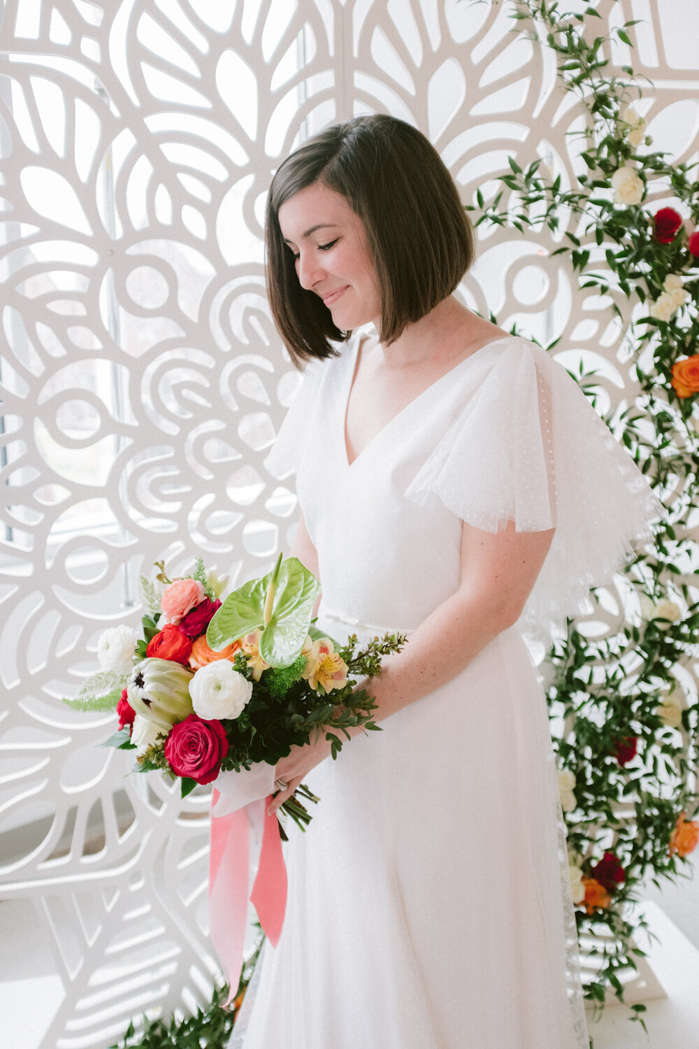 Pretty bride holding her flower bouquet in front of an elegant floral wedding backdrop