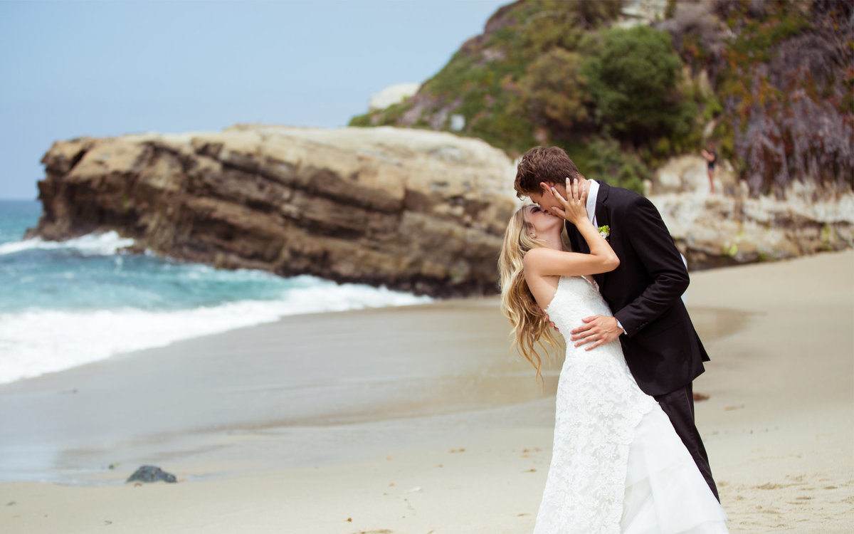 Groom dips and kisses his Bride on the sands of the California coastline