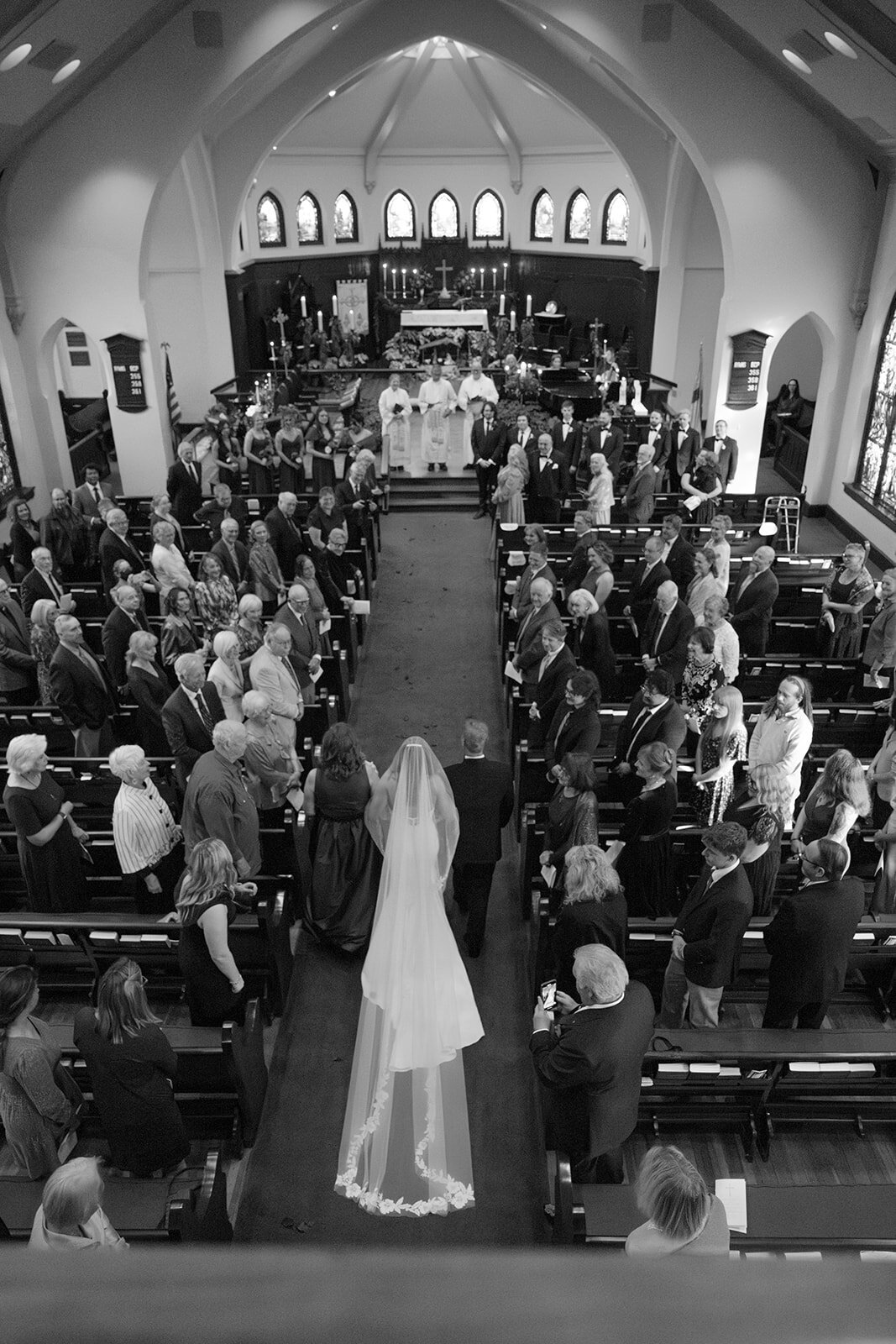 Cinematic black and white photo of bride walking down the aisle with guests watching in San Antonio church wedding
