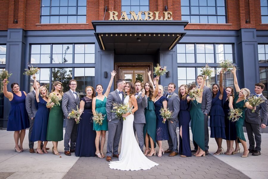 A groom whispers in his bride's ear as their wedding party throws up their hands and celebrates around them.