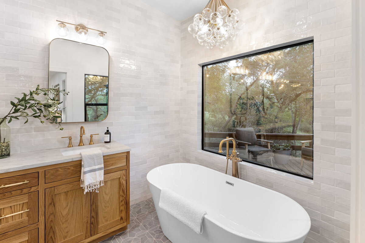 Bathroom with shiny grey tiles, large white basin and large window looking out to nature