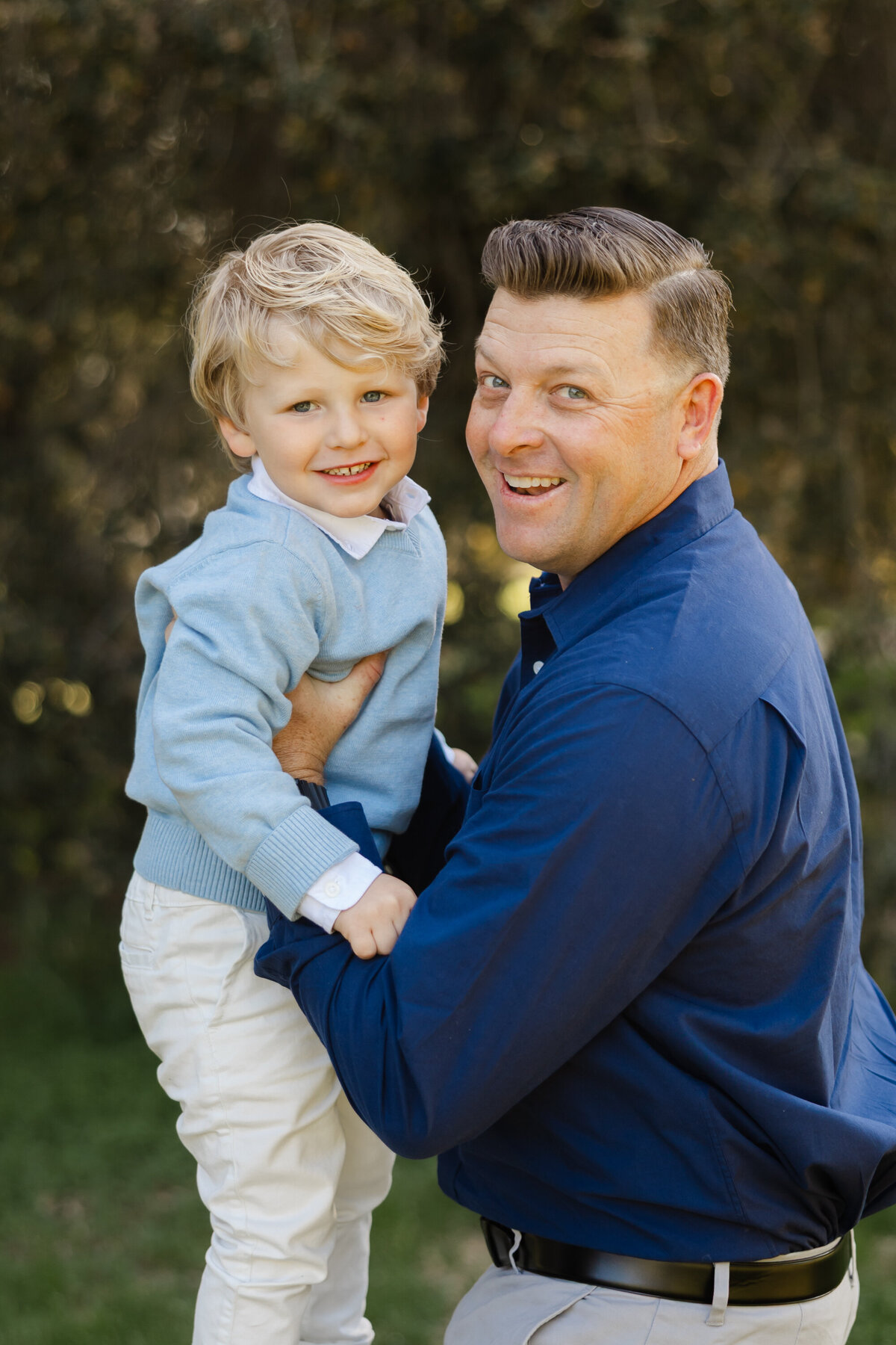 Father holding young son outdoors, both smiling in coordinated blue outfits. Photographed by Yucaipa family photographer Kaitlyn Dawn Photography.