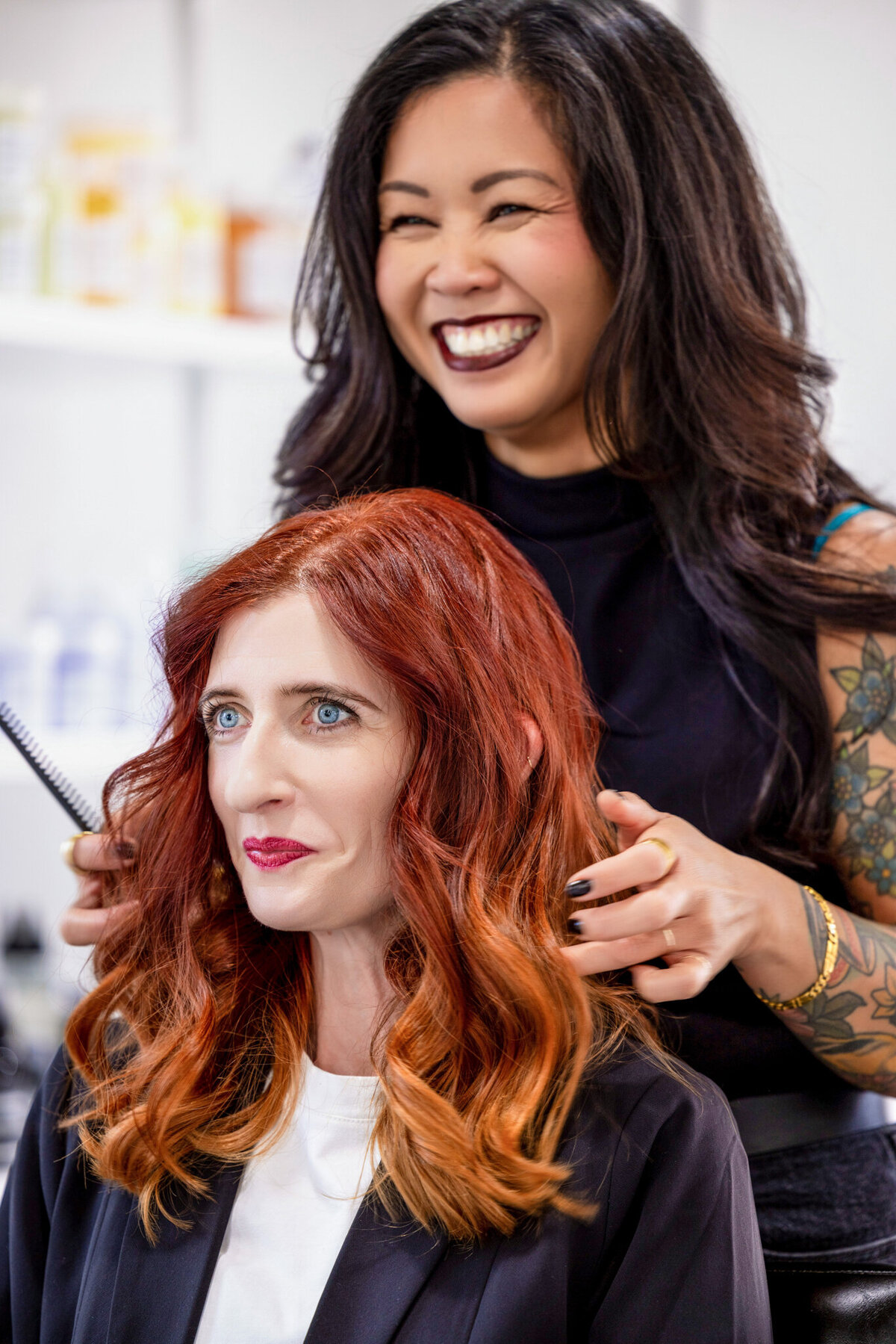 A stylish, confident hairstylist with tattooed arms perfects her client’s hair, combining artistry with precision. This shot speaks to modern, edgy salons catering to a fashion-forward clientele.