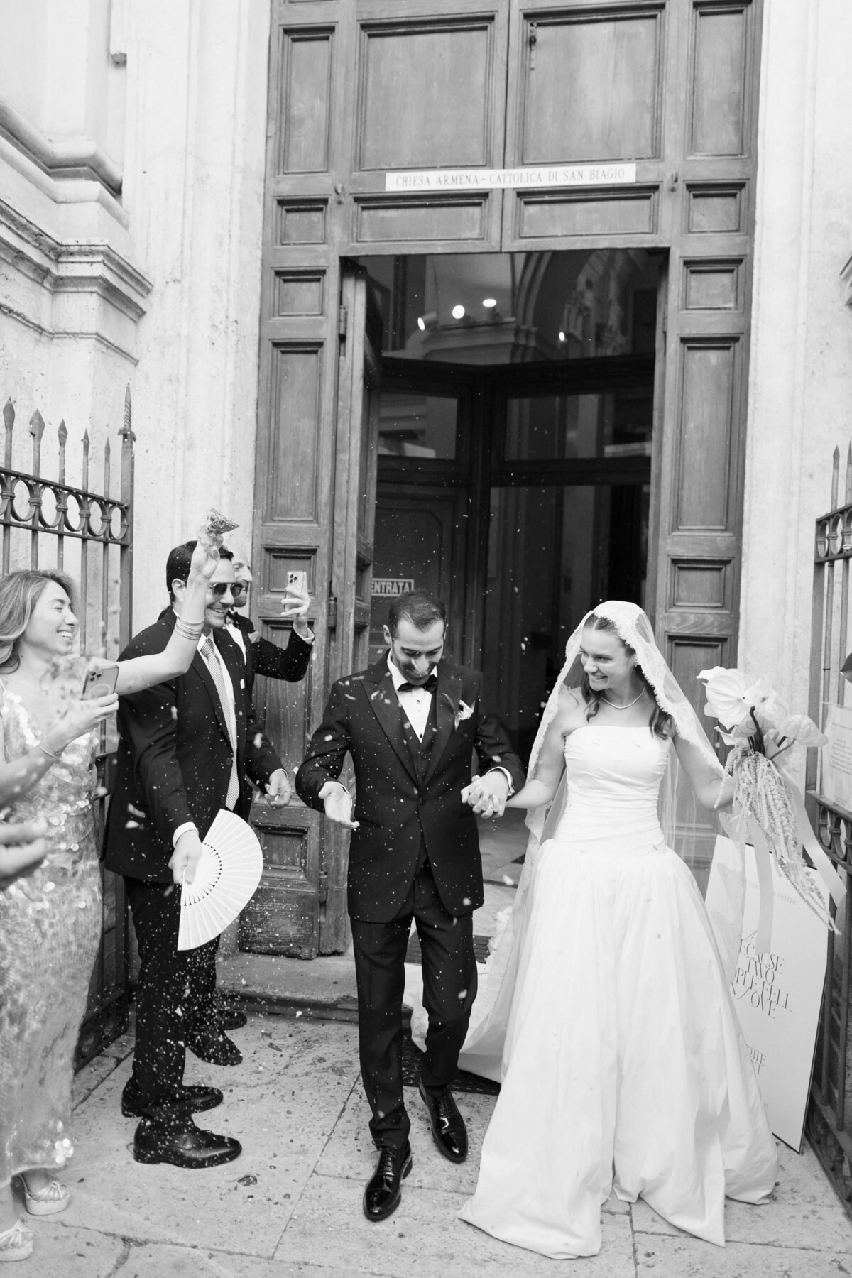 Just married couple exiting church as guests cheer and celebrate

