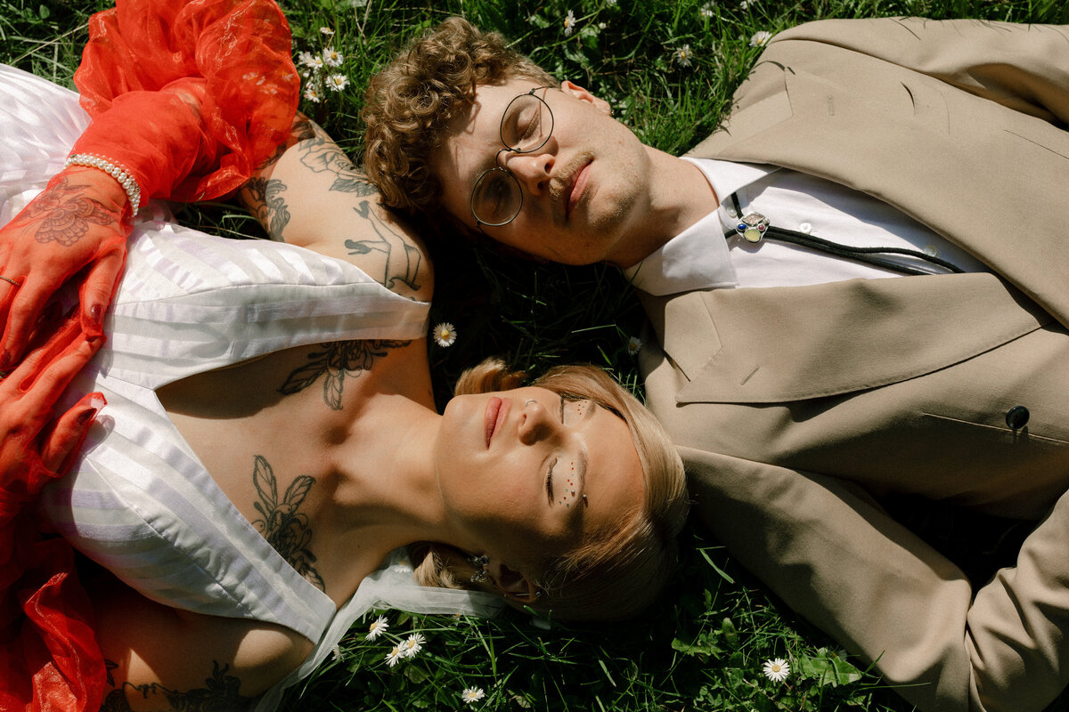 Tattooed couple lying in a field of daisies, combining alternative fashion and love in modern Seattle wedding photography.