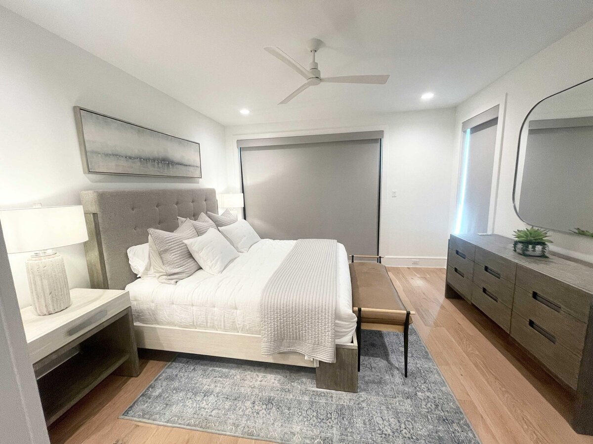 Interior design and renovation contractor for a bedroom project, using classic grey and white colors. The space is decorated with a square mirror, grey curtains, and cushions to create a sophisticated and calming atmosphere.