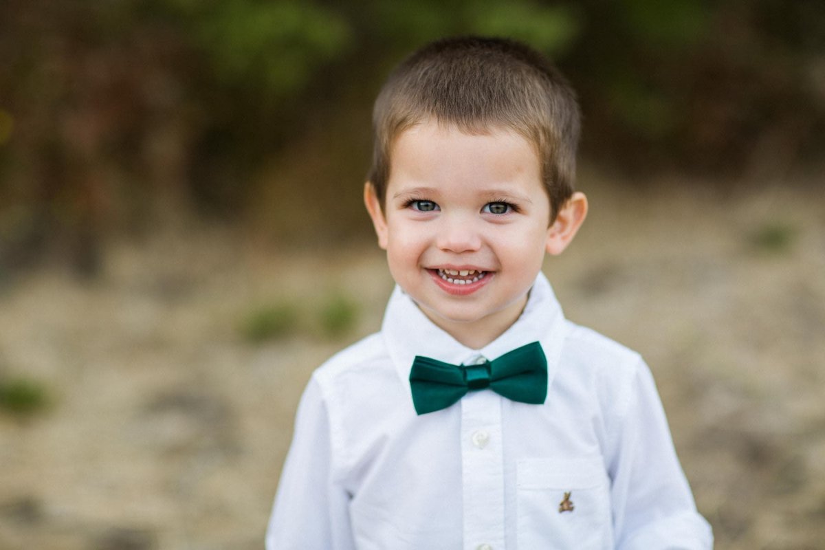 Little boy wearing a bow tie gives the photographer a big smile while posing for photos