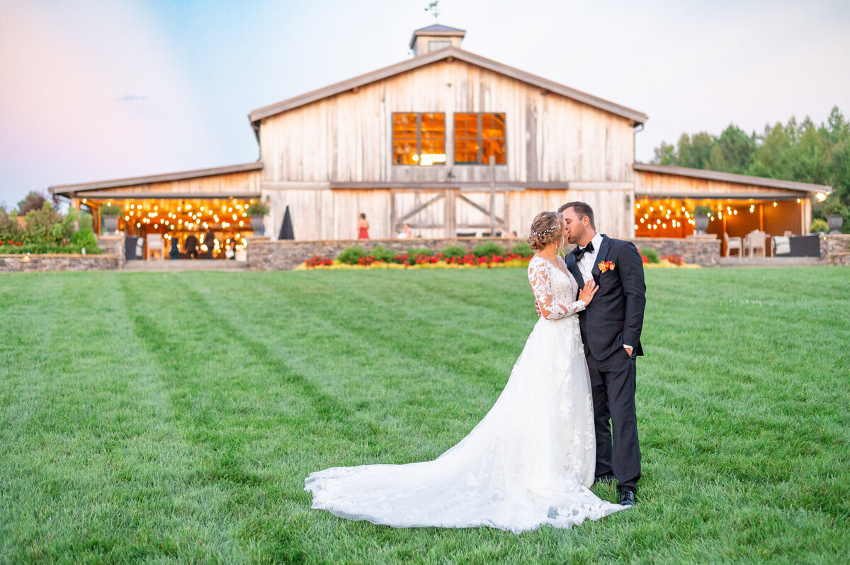 A bride and groom kissing in front of a rustic wooden barn.