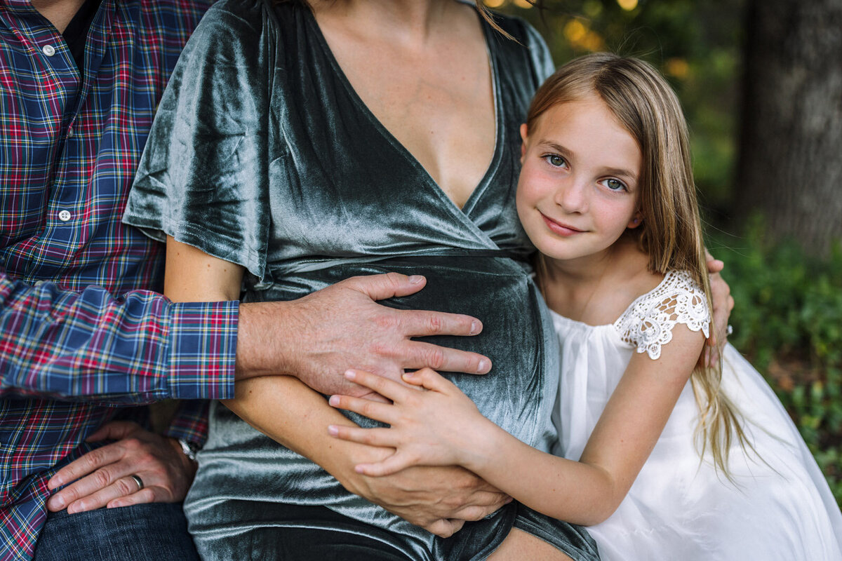 8-year-old girl sitting next to parents leaning on mom and everyone is touching mom's baby bump