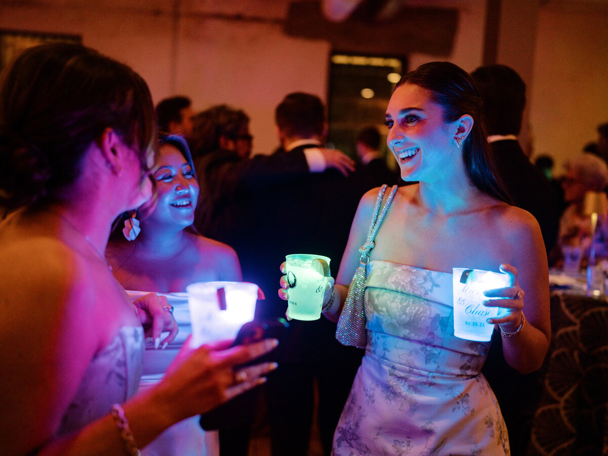 A group of joyful women share laughter and vibrant drinks in glow cups, representing the fun and energy of a lively party atmosphere filled with friendship and celebration.