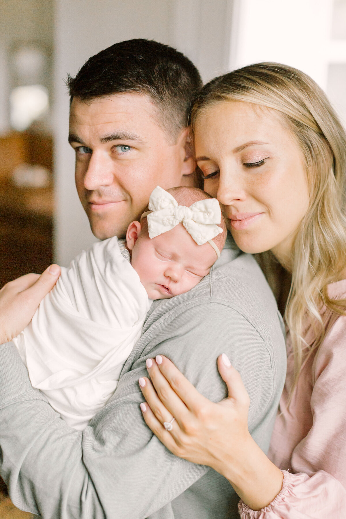 New parents holding their swaddled newborn close, capturing a cozy and emotional in-home moment — Portrait photographer in Raleigh.