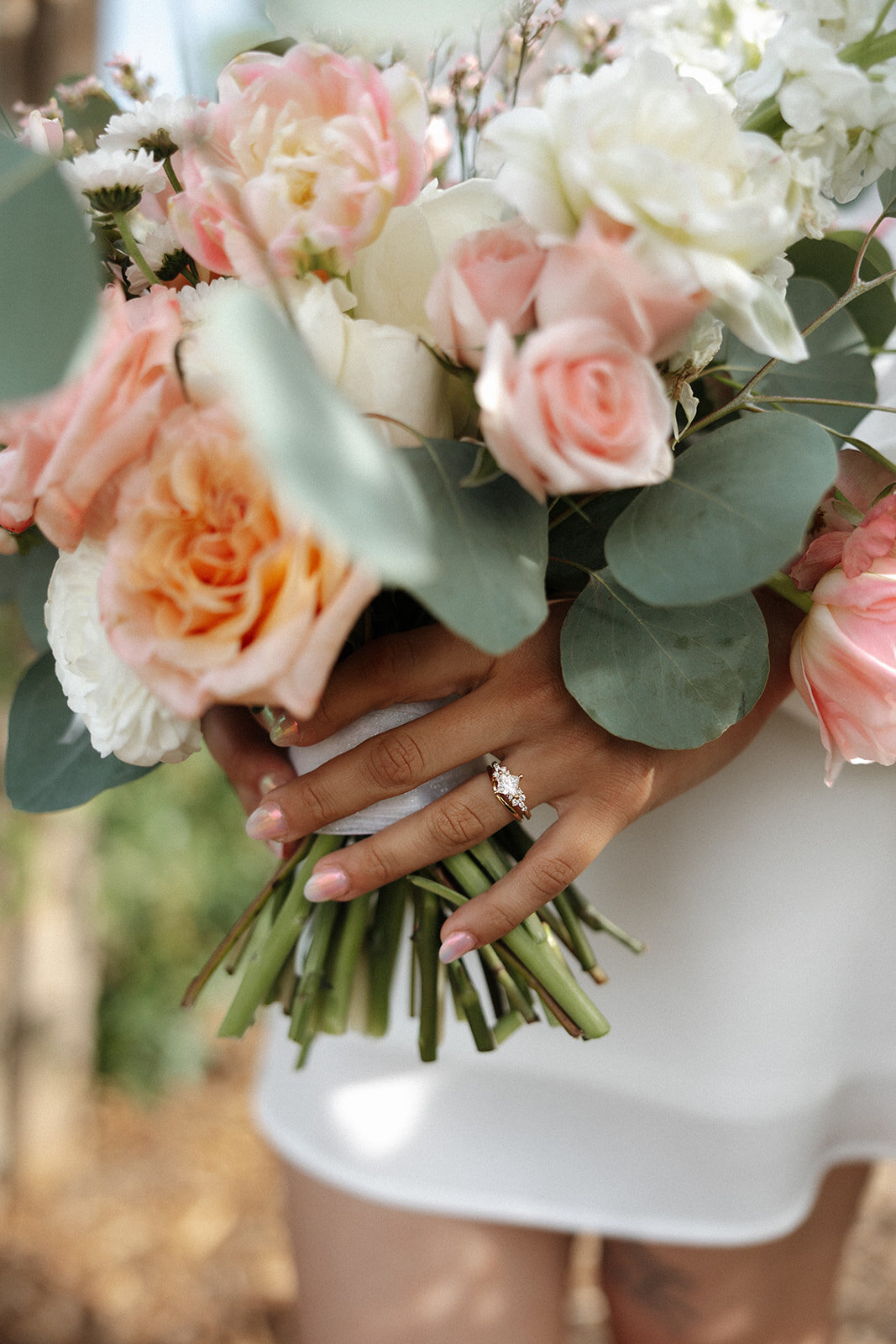A bride in Overland Park, KS, holding her bouquet with one hand while showcasing her wedding ring with the other, capturing the elegance and beauty of her special day.