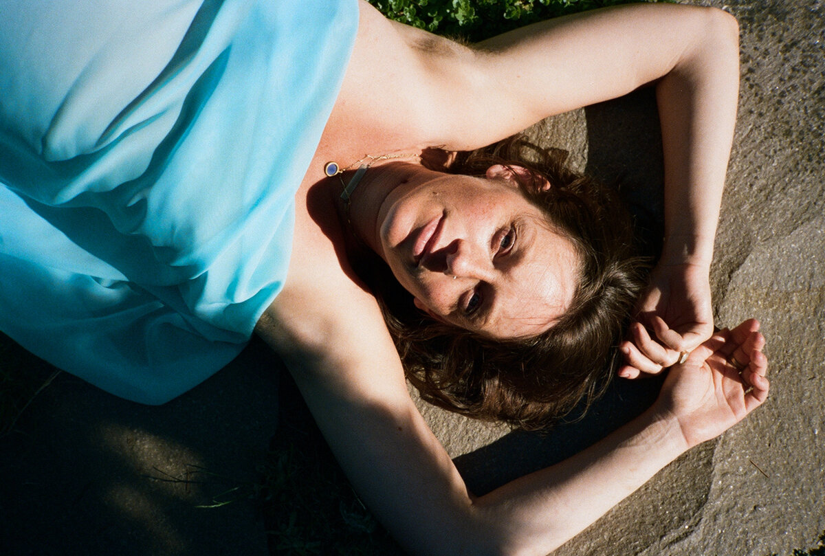 Portrait of woman laying on her back in the sun with arms overhead looking at camera