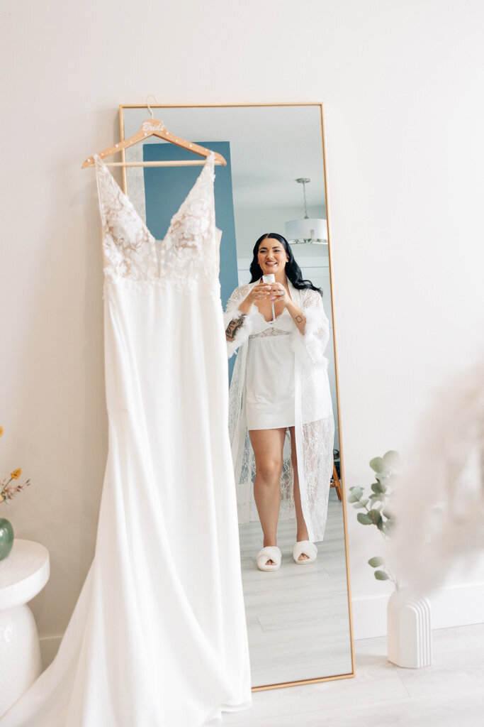 Bride admires wedding dress hanging on a floor length mirror, captured by Lorissa Lee Photography. Featured on Brontë Bride.