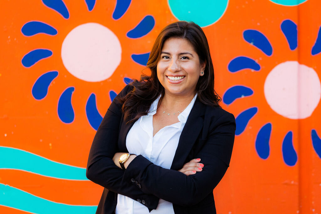 A person smiles with their arms crossed in front of a mural.