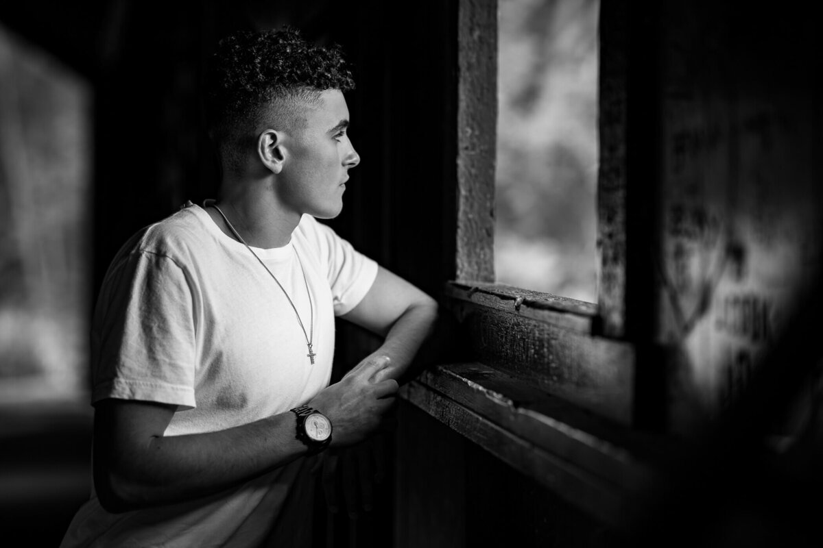 Black and white senior photo of a senior looking out the window of a covered bridge. Captured by Michael Fricke Photography, a Pittsburgh senior photographer