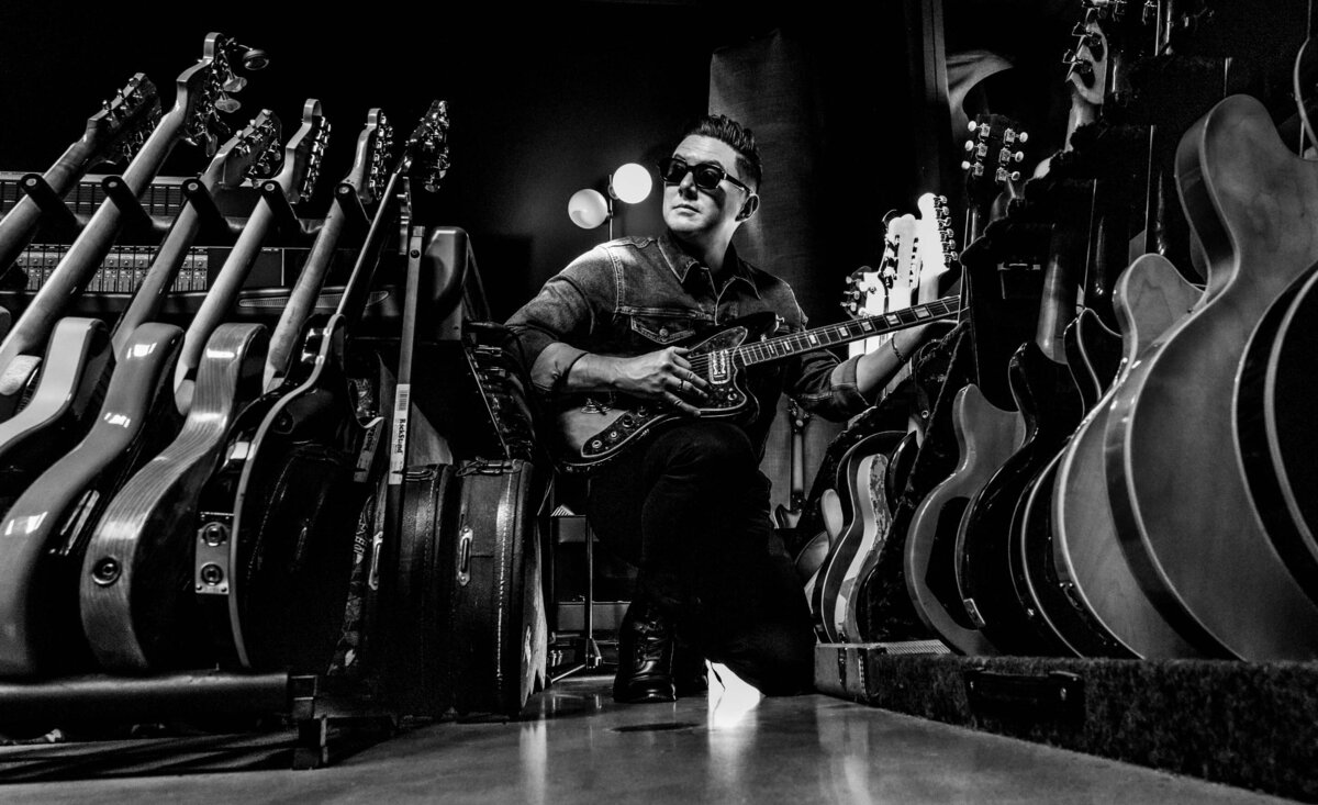 Male musician photo black and white Sean Ulbs kneeling with electric guitar between large guitar stacks