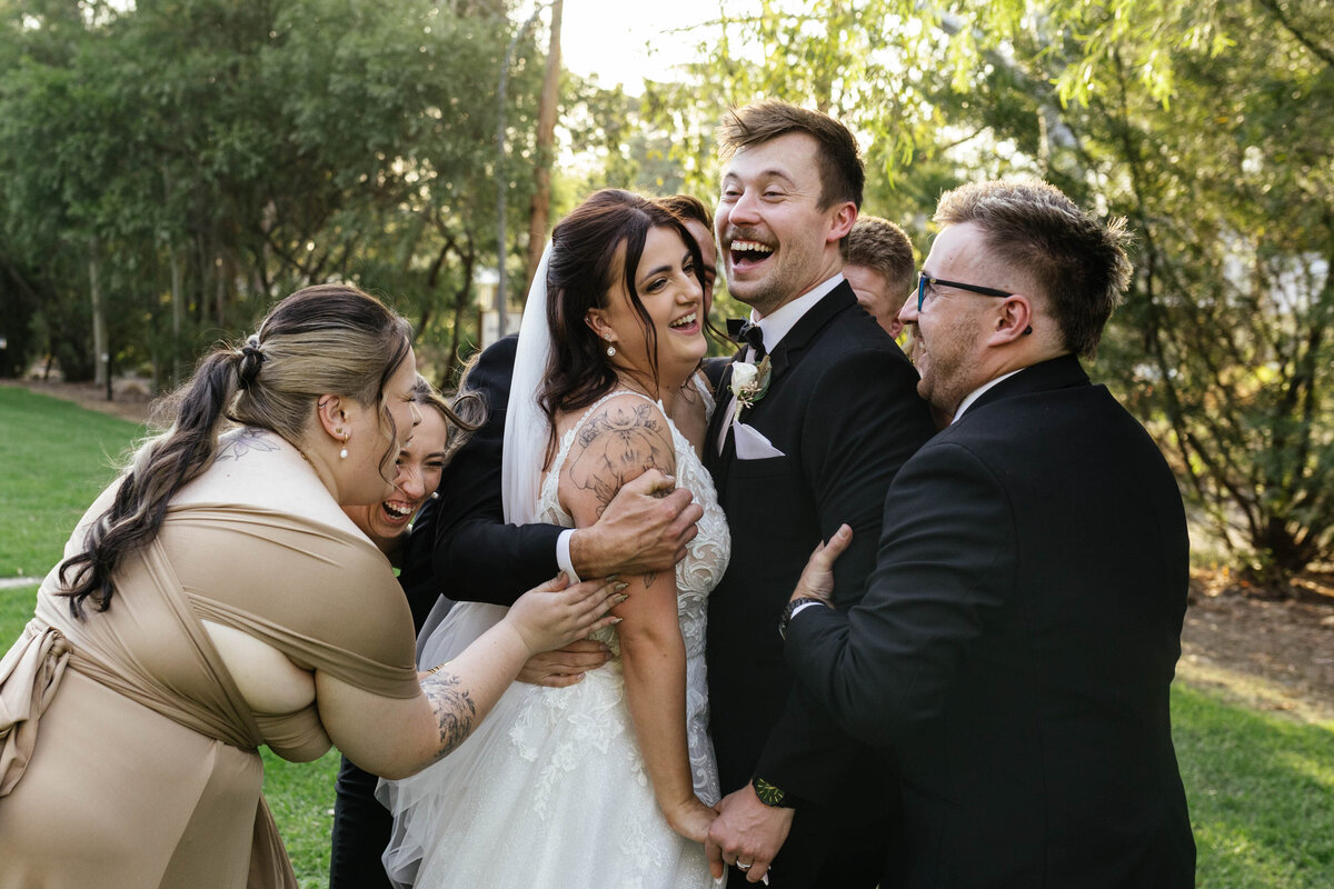 The playful bridal party all lean in for a big hug, surrounding the bride and groom, causing a natural burst of laughter from the Bride & Groom. 