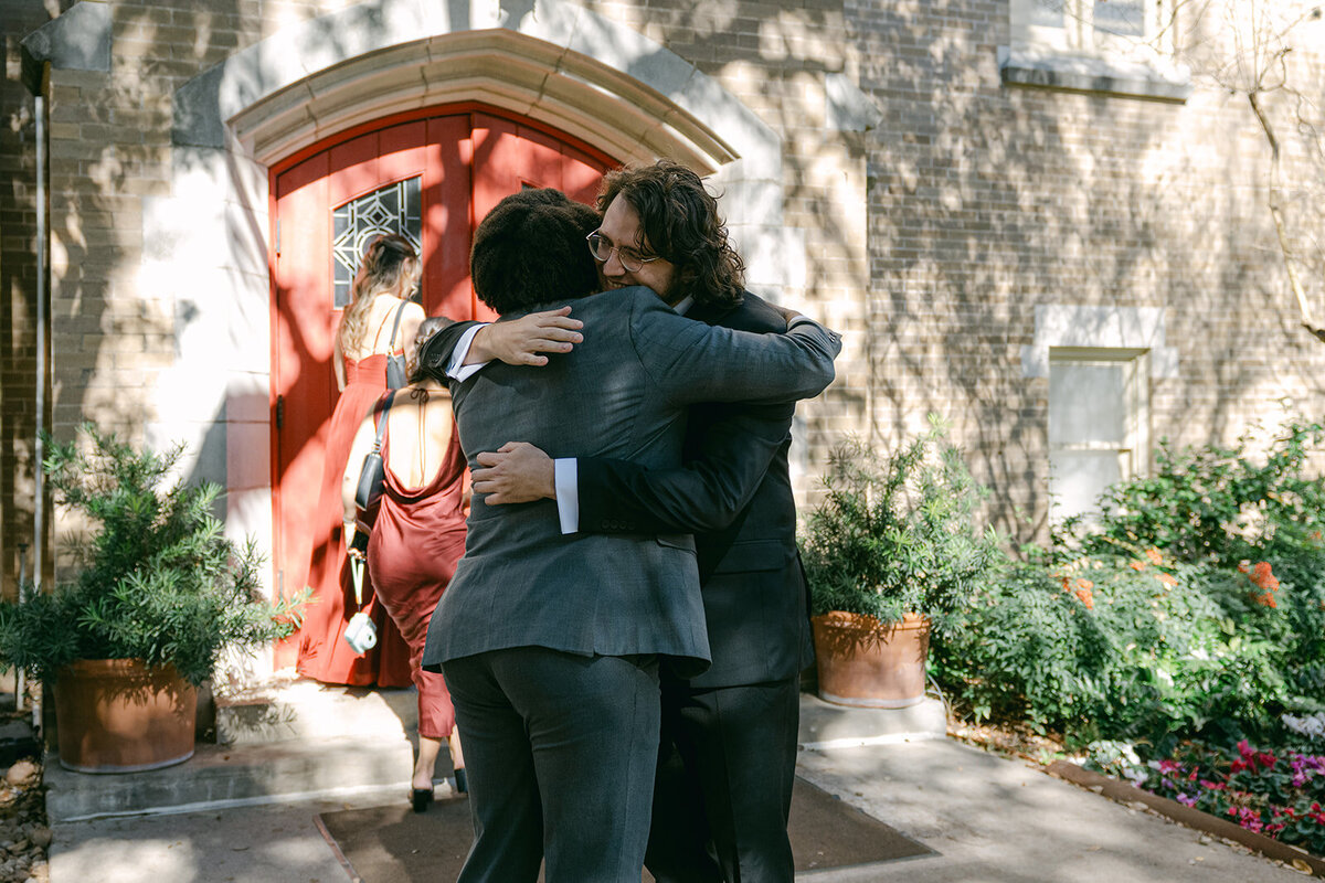 Joyful welcome hug at the arrival of guest and groom outside of a luxury church wedding