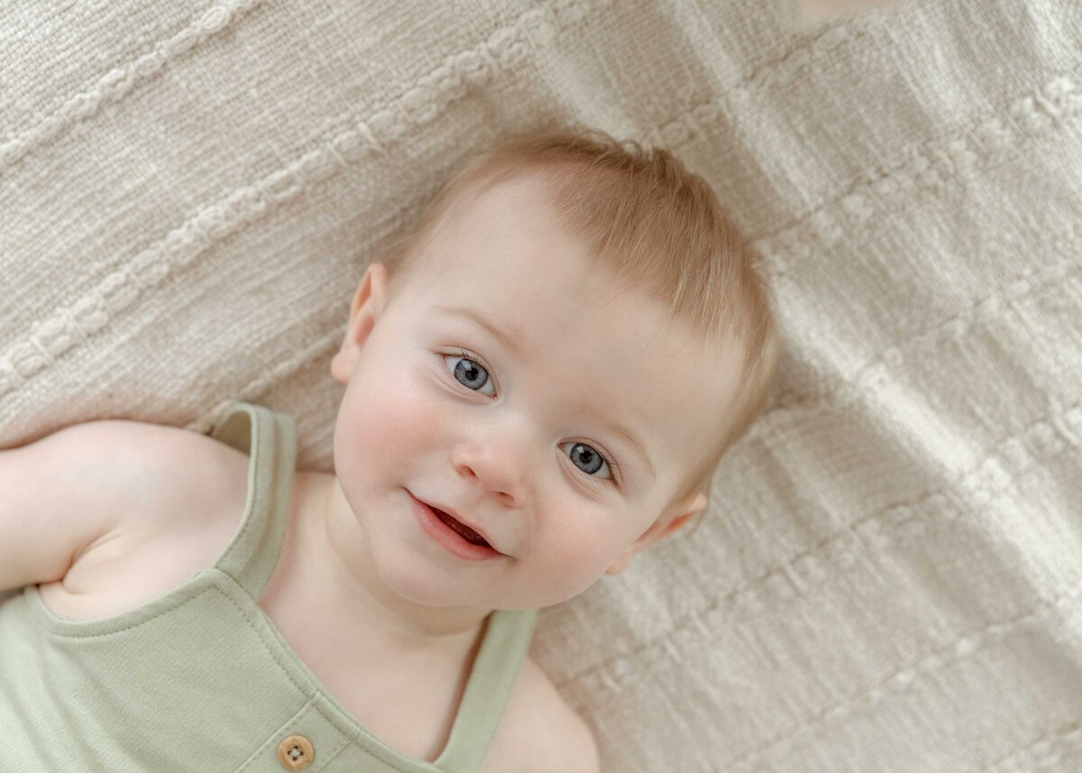 Close up image of one year old boy laying on bed, dressed in sage overalls