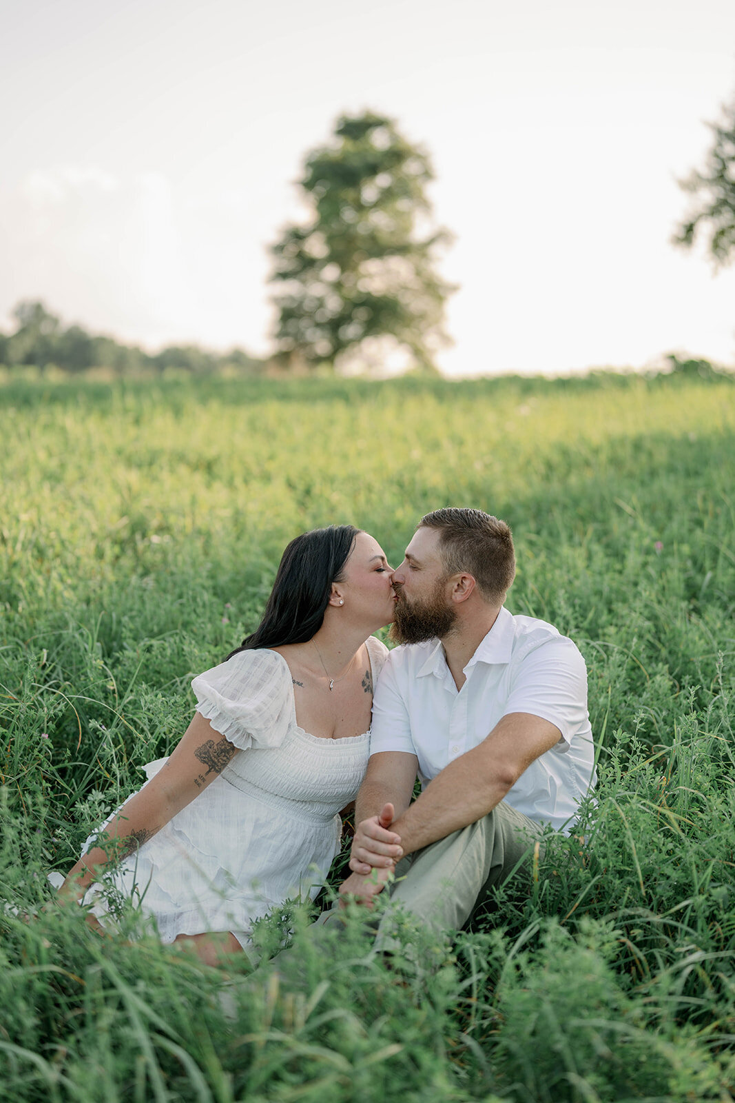 Close-up of Kali and Joe sharing a kiss while sitting in tall grass during their Detroit engagement photos.