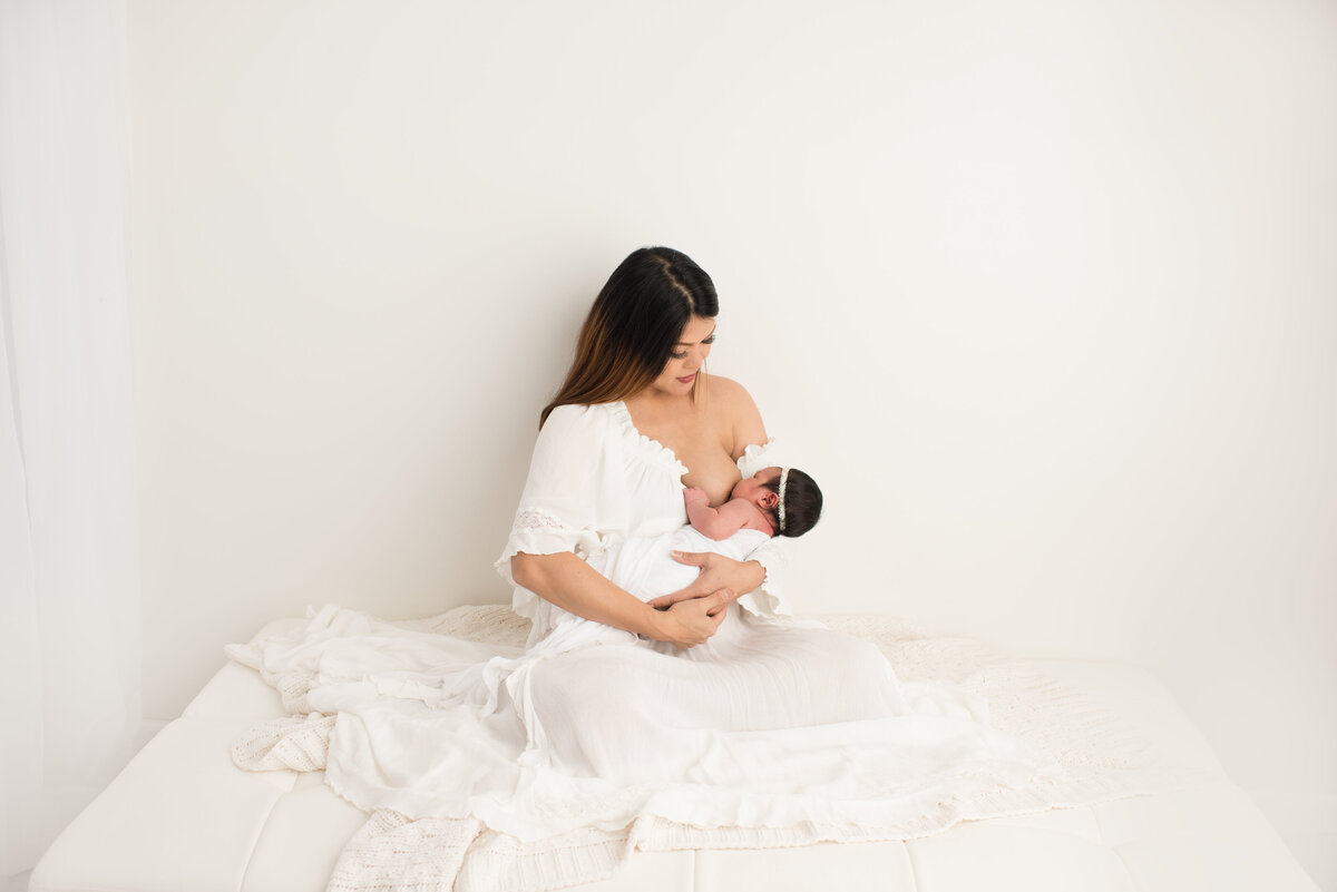 newborn feeding on mom in a family session with all white background