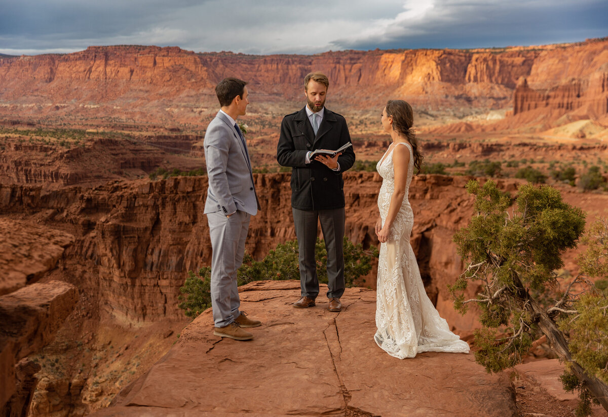 Bride and Groom with their officiant during their ceremony on a red cliff overlook at Capitol Reef National Park in Utah