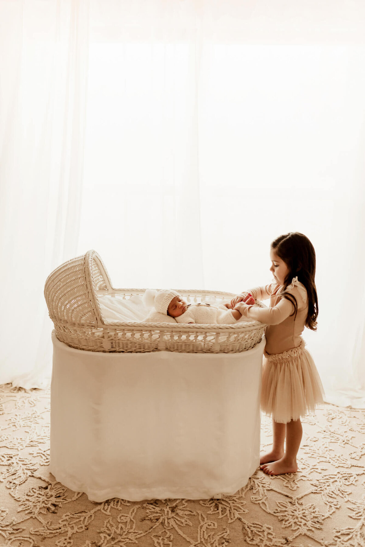 Pottery barn bassinet with a newborn baby boy and a big sister looking into the bassinet at her brother, lifestyle newborn session in OKC.