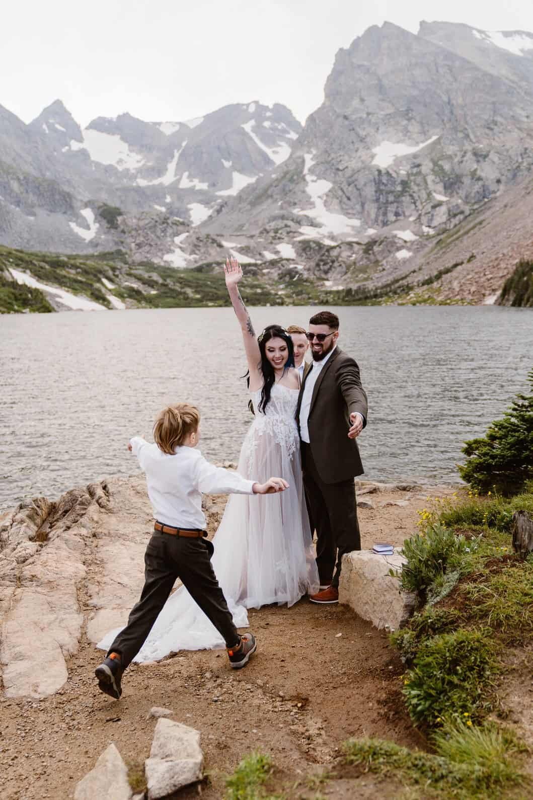Bride and groom celebrate their child runs toward them after their mountain lake elopement ceremony in Colorado.