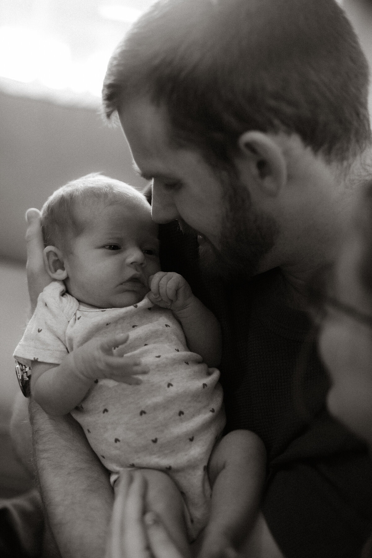 A father gazes at his baby lovingly, their faces close together as he cradles the baby in his arms.