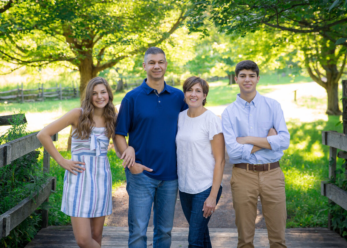 family portrait on wooden bridge with greenery in the background