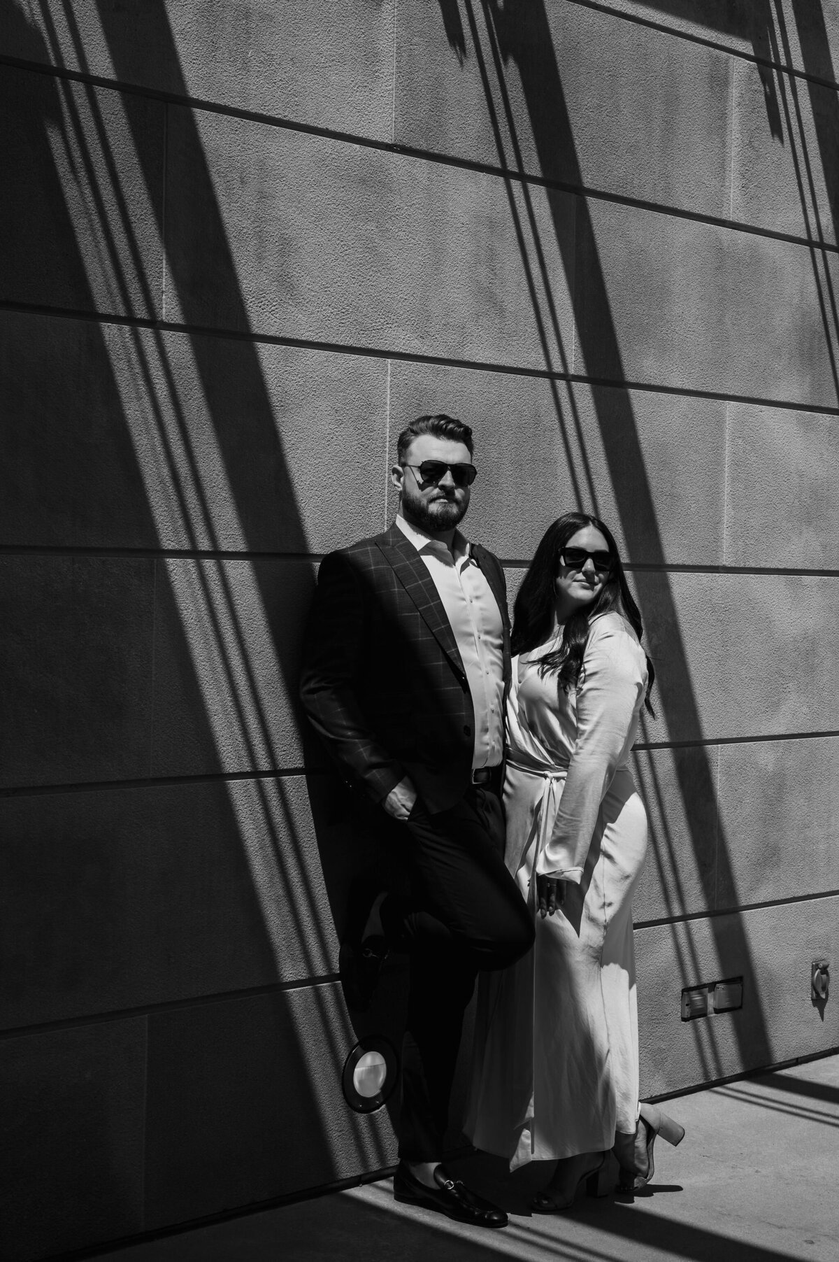A couple wearing sunglasses lean against cement wall