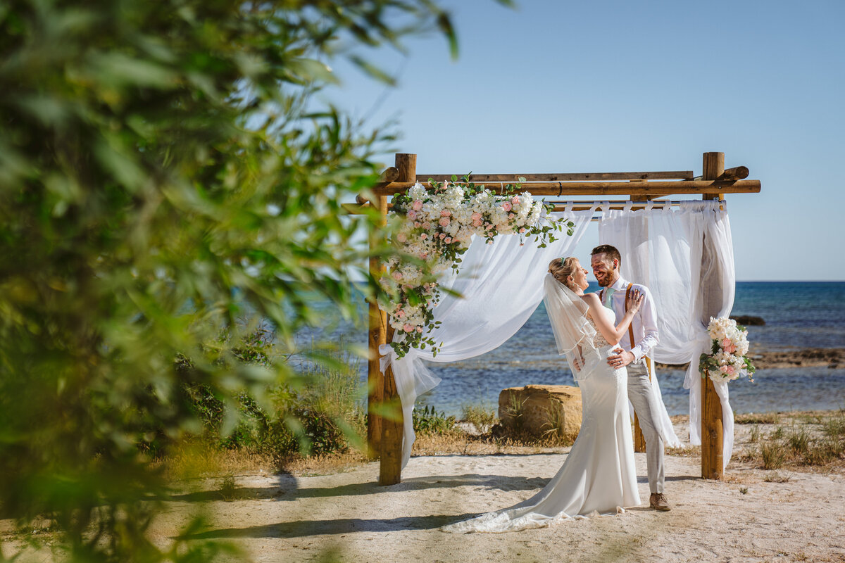 Couple kiss infront of the decorated gazebo on the beach at their wedding