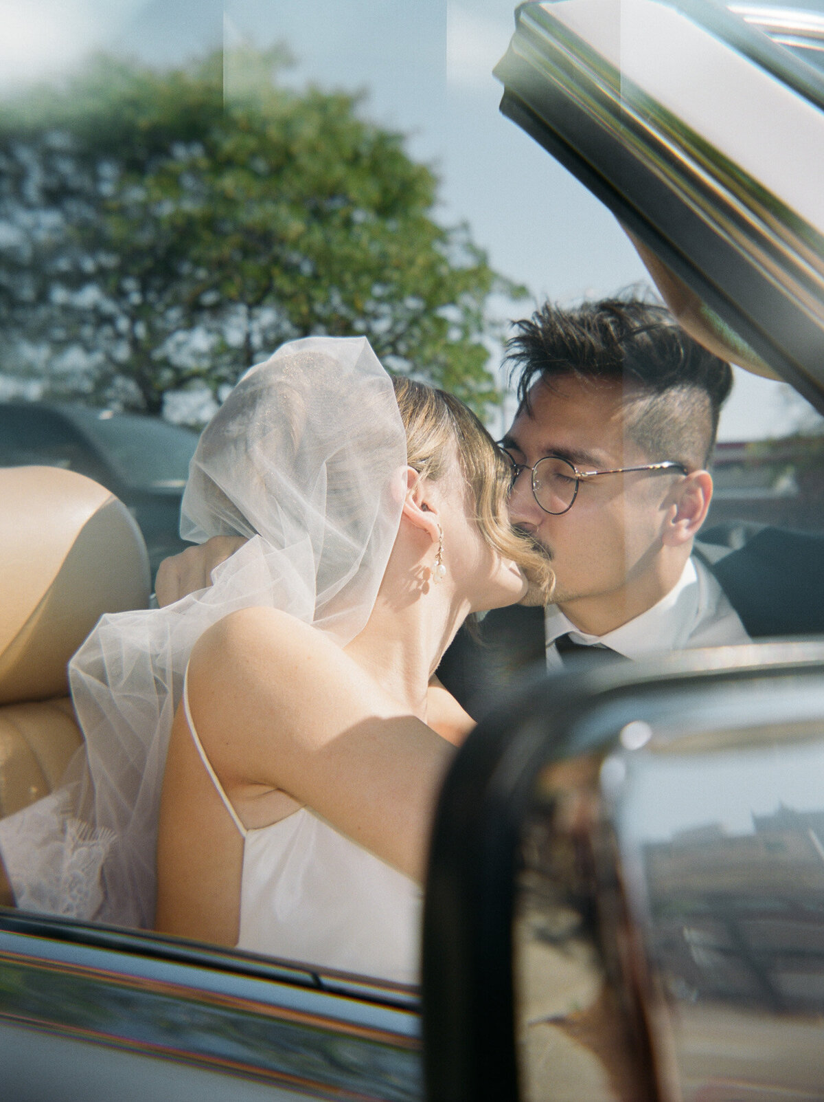 soft film photo of newlywed bride and groom, kiss in vintage car on wedding day