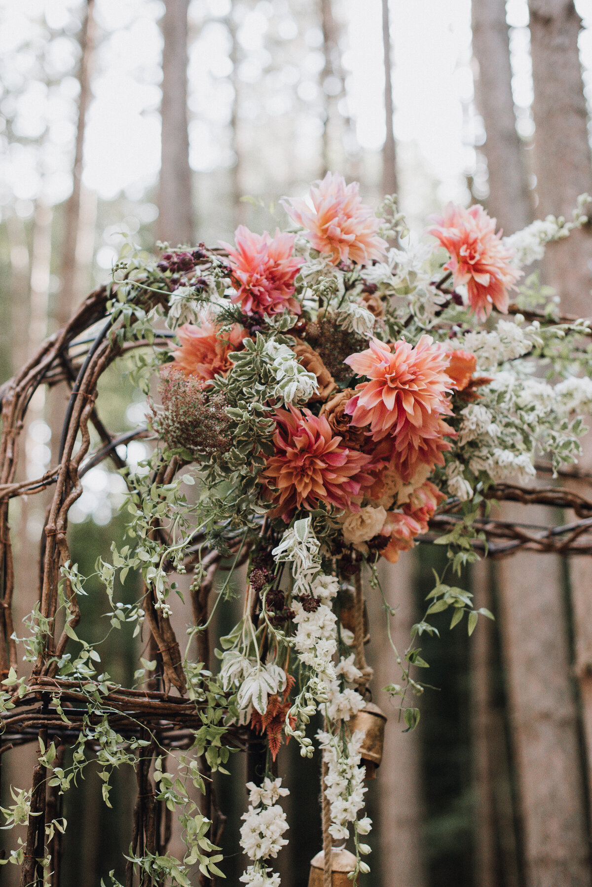 Detail of a wicker wedding arbor with copper dahlias , white larkspur, and greenery standing in a forest