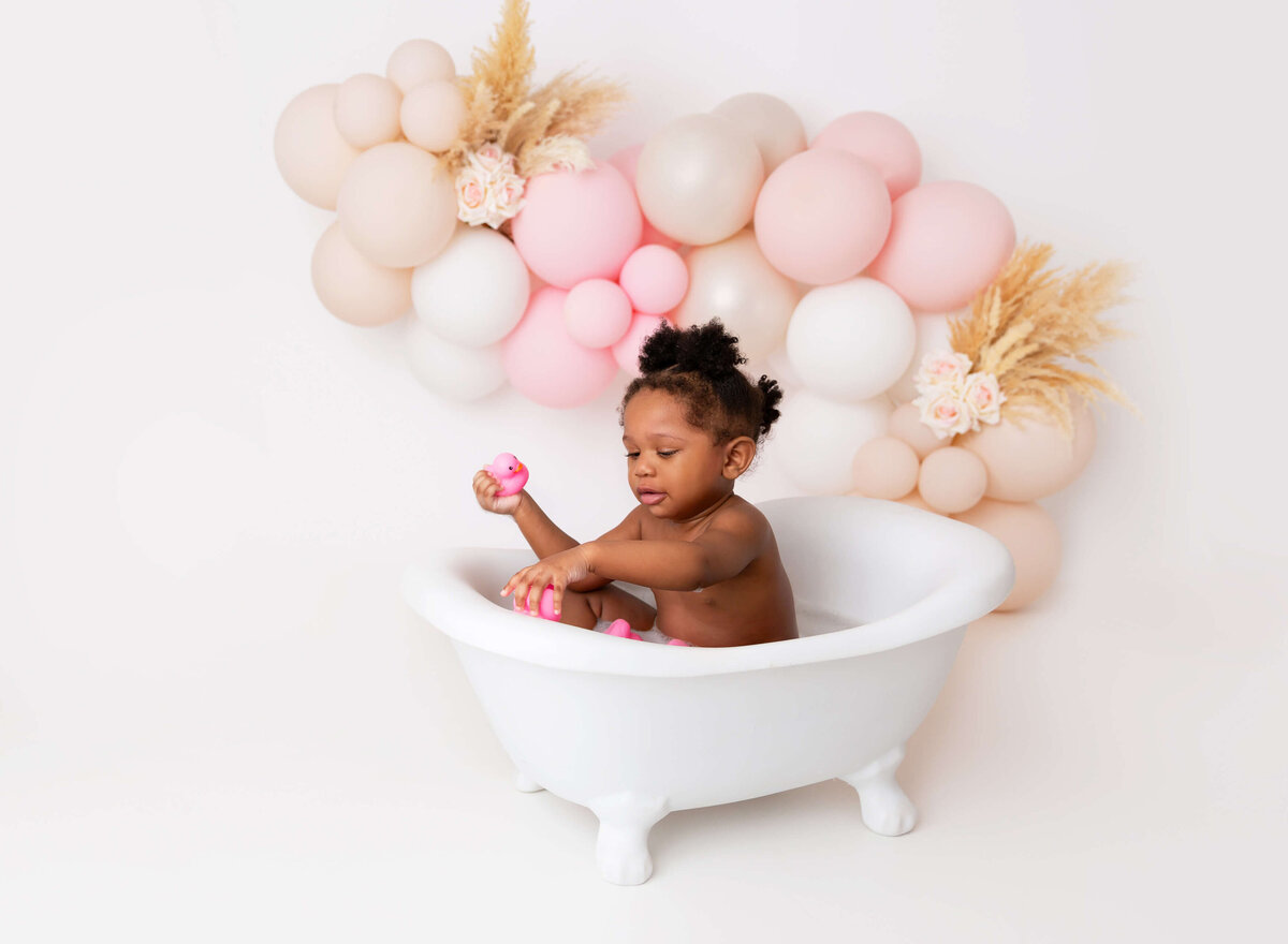Baby girl in the bubble bath tub for her cake smash session pink whiye and beige balloon garland
