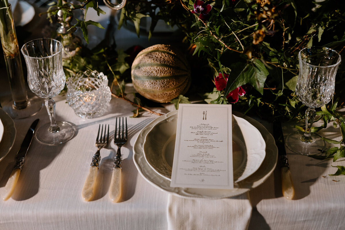 A wedding reception table set with flatware and small plants and fruits 