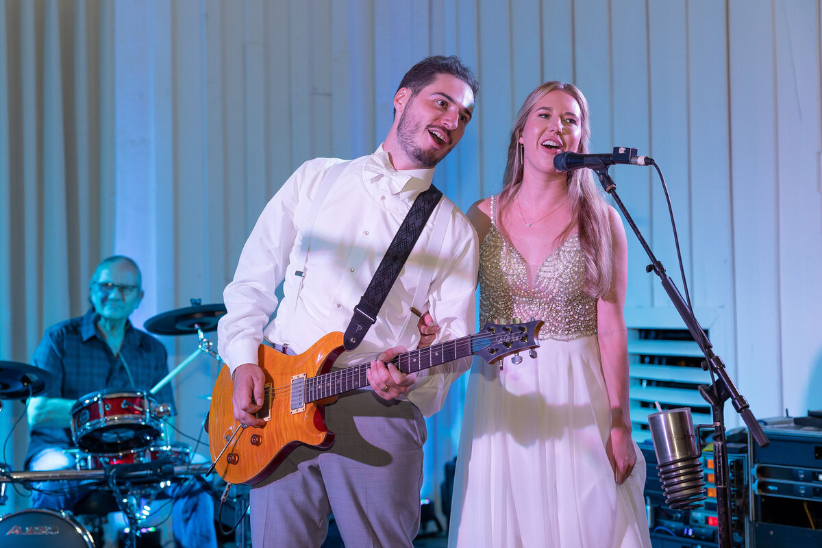 groom holds guitar and sings with bride at microphone on stage at Milestone Georgetown wedding