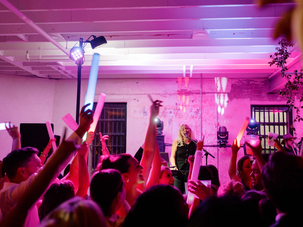 An electrifying atmosphere at wedding reception where the guests enthusiastically engages with live music, cheering and waving illuminated props, celebrating the vibrant experience together.