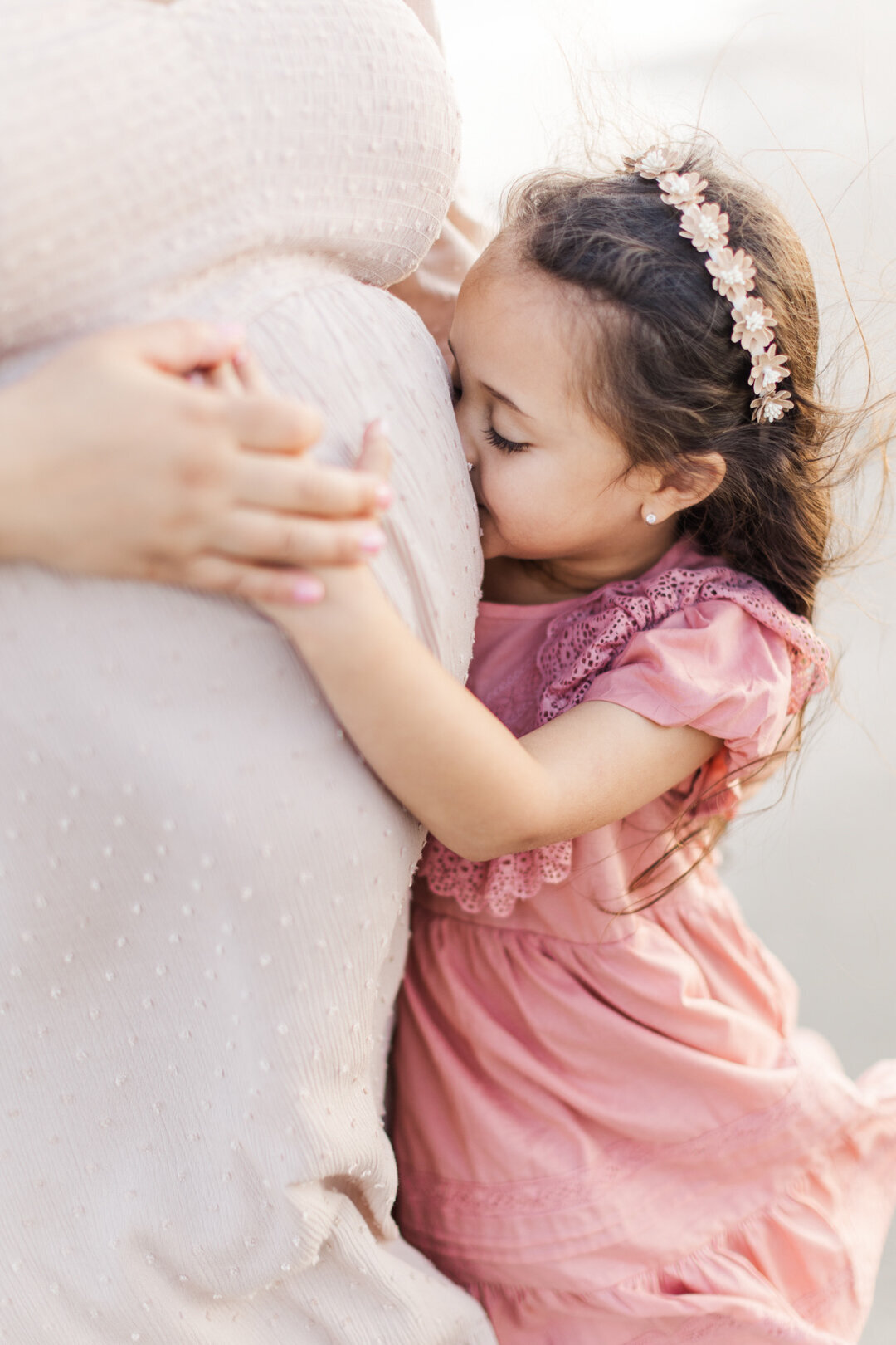 daughter kisses moms pregnant belly for maternity photo session