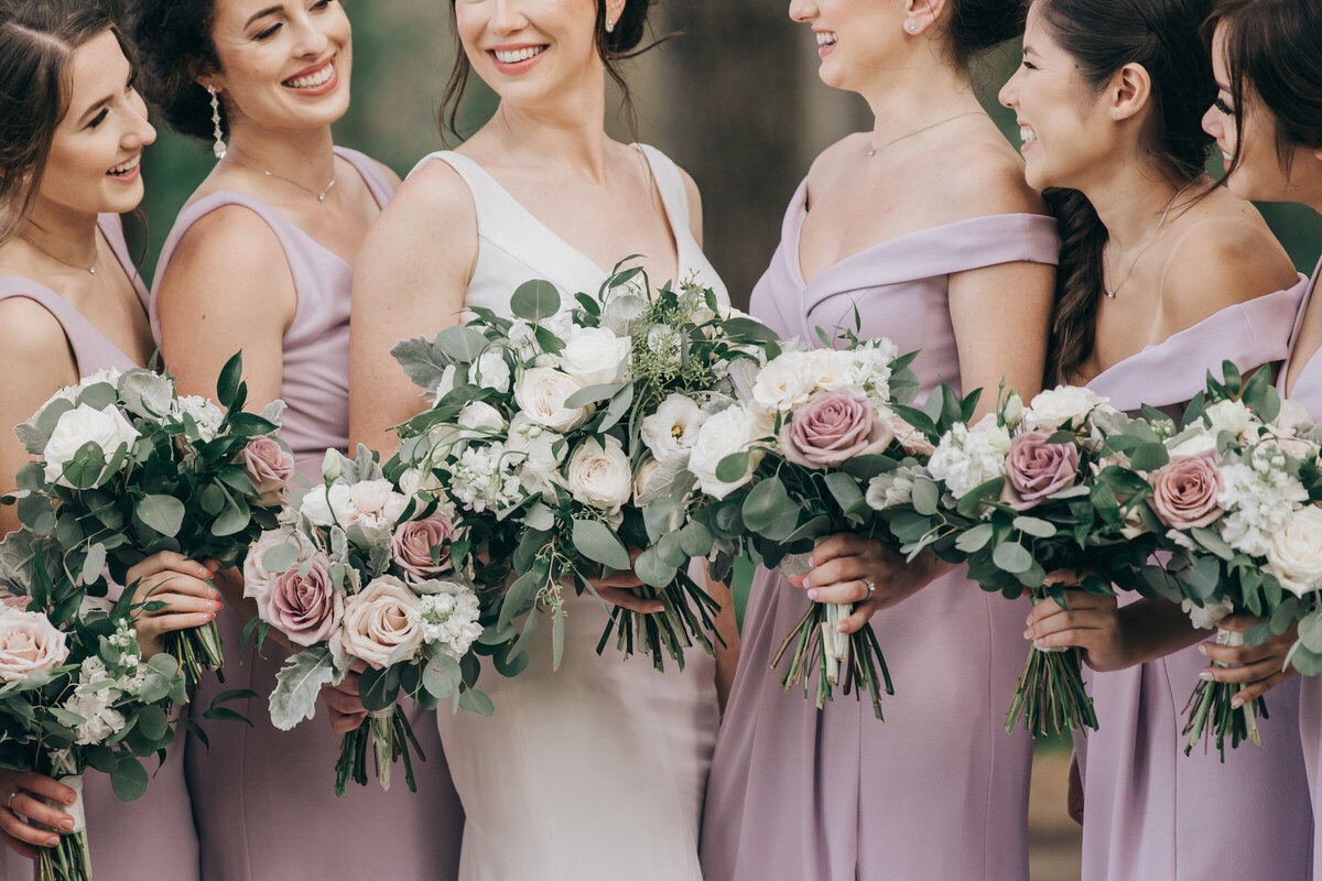 Elegant bridesmaids wearing lavender dresses and holding gorgeous bouquetswhile posing for photos in an enchanted forest