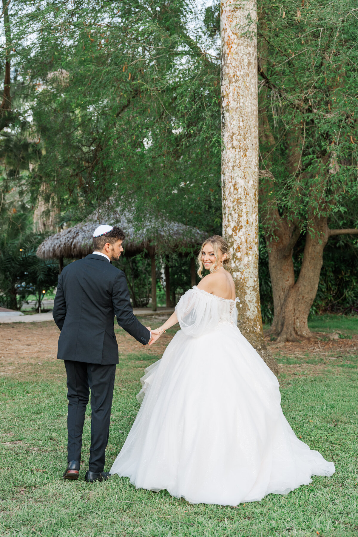 bride and groom walking away frm the camera while she looks bak at it
