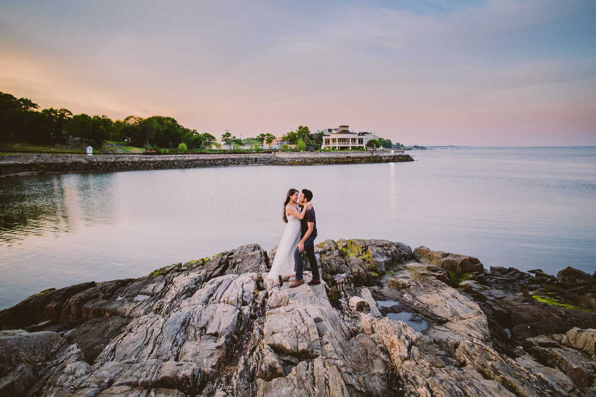 engaged couple embrace on a rock near the water at orchard beach in the bronx 
