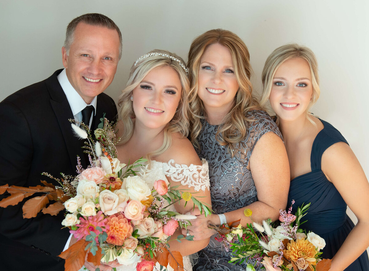 a family photo of a bride with her mom, dad and sister as they get ready for her Ottawa wedding.  The bride and her sister are holding fall coloured bouquets