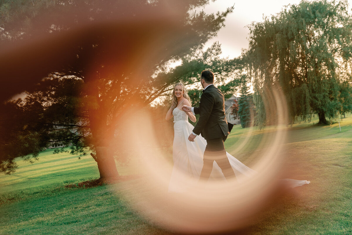 candid shot of bride and groom walking across lush green grass