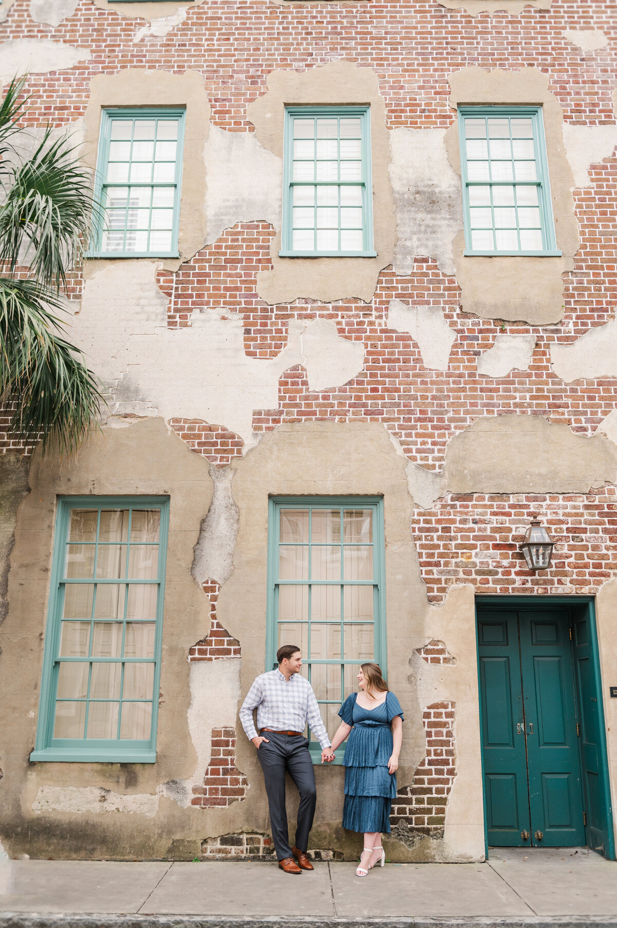 couple holding hands with a beautiful building in charleston, sc